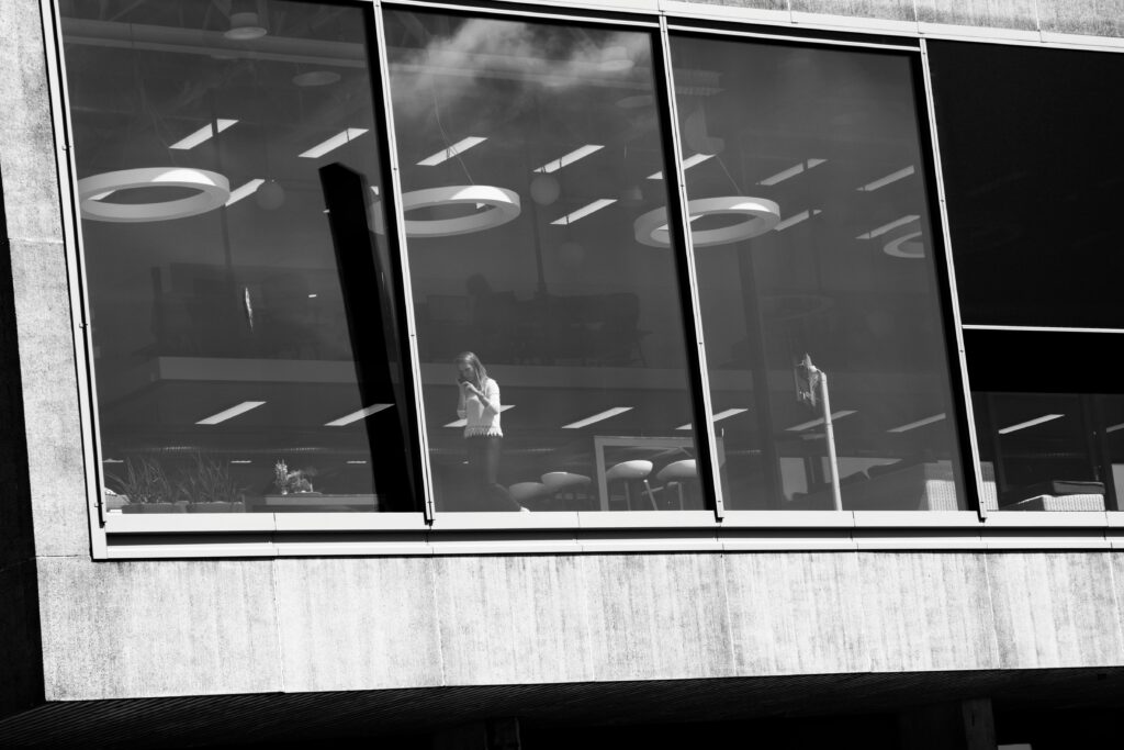 Black and white photo of a modern office building's glass facade featuring reflections and interior details.
